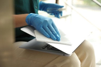 Woman in latex gloves cleaning laptop with wet wipe indoors, closeup