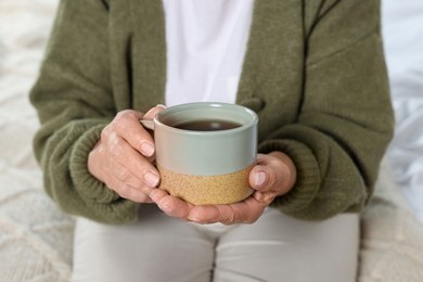 Elderly woman with cup of hot drink indoors, closeup. Home care service