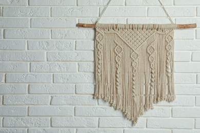 Beautiful macrame hanging on white brick wall, space for text. Decorative element