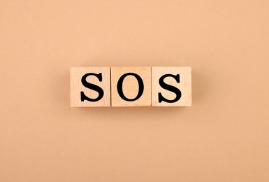 Abbreviation SOS made of wooden cubes on light brown background, top view