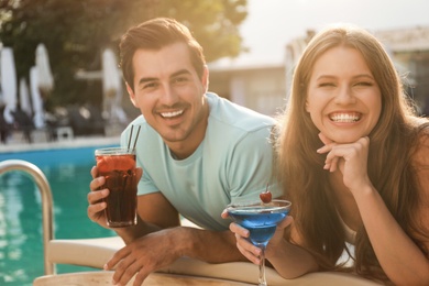 Happy young couple with fresh summer cocktails relaxing near swimming pool