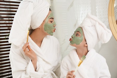 Young mother and her daughter with facial masks having fun in bathroom