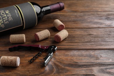 Corkscrew, wine bottle and stoppers on wooden table. Space for text