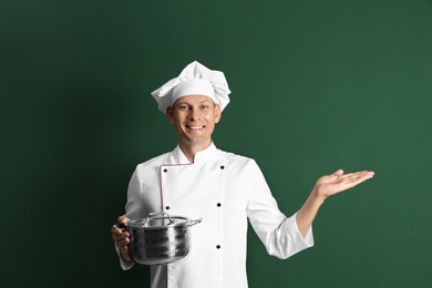 Happy male chef with cooking pot on dark green background