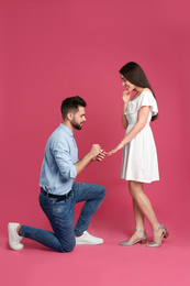 Man with engagement ring making marriage proposal to girlfriend on crimson background