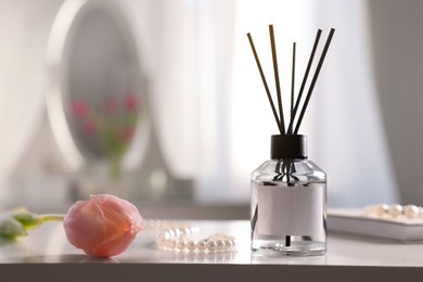 Reed diffuser, beautiful flower and pearl necklace on white table indoors. Space for text
