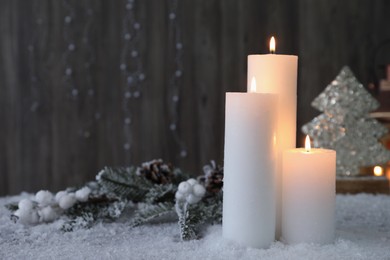 Burning candles and Christmas decor on artificial snow. Space for text