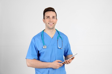 Portrait of medical assistant with stethoscope and tablet on light background
