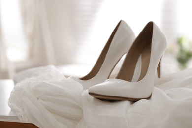 Pair of white high heel shoes and wedding dress on table indoors