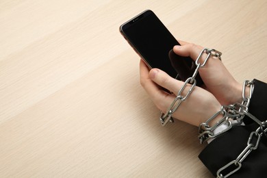Man holding smartphone in chained hands at wooden table, above view. Internet addiction