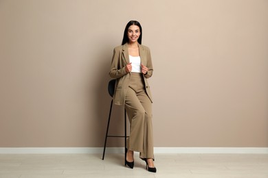 Beautiful young businesswoman sitting on stool near beige wall