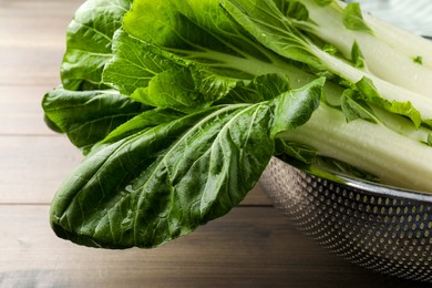 Fresh green pak choy cabbages with water drops in colander on wooden table, closeup