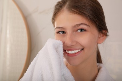 Beautiful teenage girl wiping face with towel at home, closeup