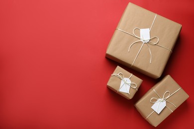 Photo of Parcels wrapped in kraft paper with tags on red background, flat lay. Space for text