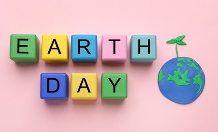 Phrase Earth Day made with cubes and model of planet on pink background, flat lay