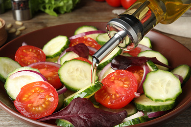 Adding cooking oil to delicious salad on table, closeup