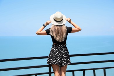 Woman with hat near sea on sunny day, back view