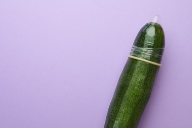 Cucumber with condom on lilac background, top view and space for text. Safe sex concept