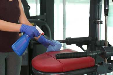 Woman cleaning exercise equipment with disinfectant spray and cloth in gym, closeup