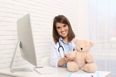 Pediatrician with teddy bear at table in clinic