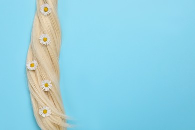 Lock of healthy blond hair with flowers on light blue background, top view. Space for text