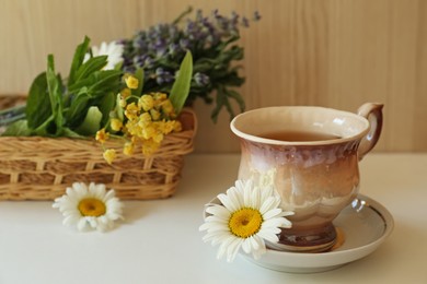 Photo of Tasty herbal tea and fresh chamomile flowers on white table, space for text