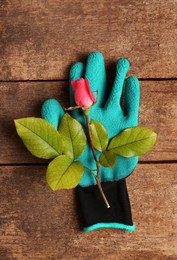 Photo of Gardening gloves with beautiful rose on wooden table, top view