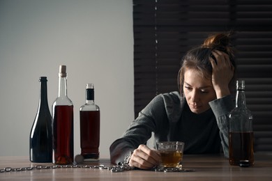 Alcohol addiction. Woman chained with glass of liquor at wooden table in room