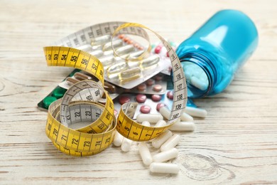 Many different weight loss pills and measuring tape on white wooden table
