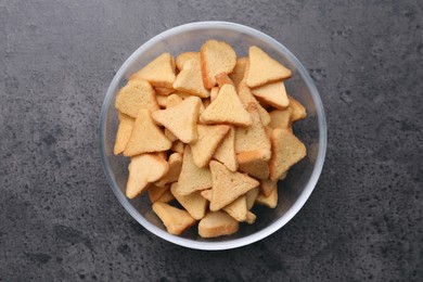 Crispy rusks in bowl on grey table, top view