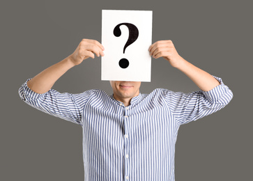 Man holding paper with question mark on grey background