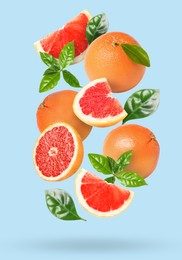 Tasty ripe grapefruits and green leaves falling on light blue background