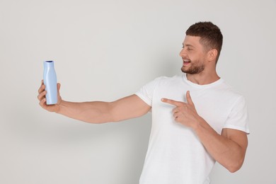 Handsome young man holding bottle of shampoo on white background
