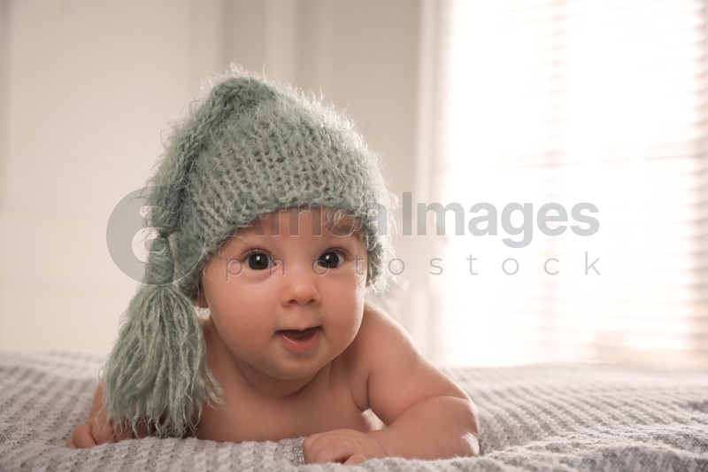 Cute little baby wearing knitted hat on bed at home, space for text