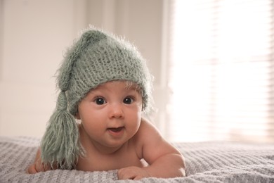 Photo of Cute little baby wearing knitted hat on bed at home, space for text