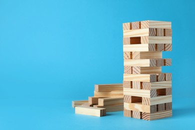 Jenga tower and wooden blocks on light blue background, space for text