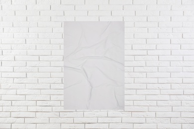 Blank creased poster on white brick wall. Mockup for design 