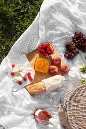 Picnic blanket with tasty food, flowers, basket and cider on green grass outdoors, flat lay