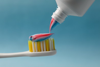 Squeezing toothpaste onto brush against light blue background, closeup