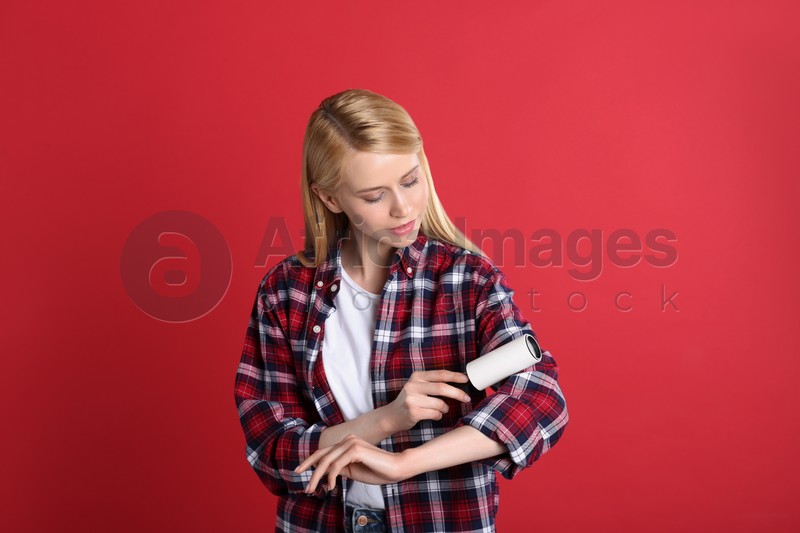 Photo of Young woman cleaning clothes with lint roller on red background