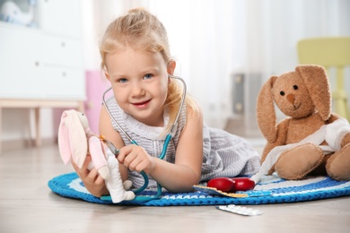 Cute child imagining herself as doctor while playing with stethoscope and toy bunny at home