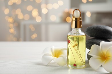 Photo of Beautiful spa composition with essential oil and plumeria flowers on white table against blurred lights, space for text