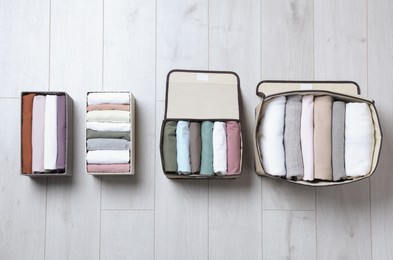 Textile cases and boxes with folded clothes on white wooden background, flat lay. Vertical storage