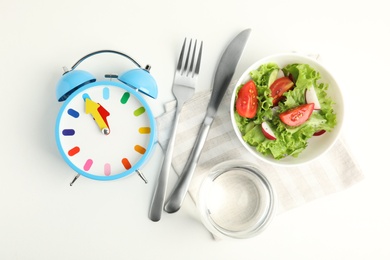 Alarm clock and salad on white background, top view. Meal timing concept