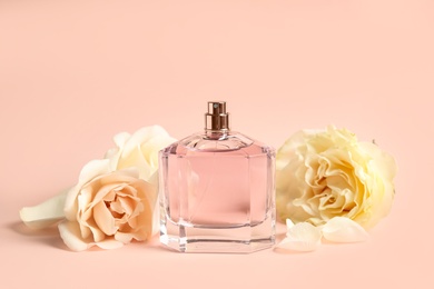 Bottle of perfume and beautiful flowers on beige background