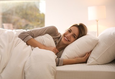 Photo of Cheerful woman under warm white blanket lying in bed indoors