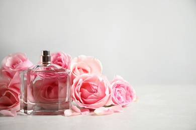 Bottle of perfume and beautiful roses on light table. Space for text