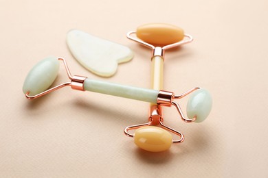 Photo of Gua sha stone and different face rollers on beige background