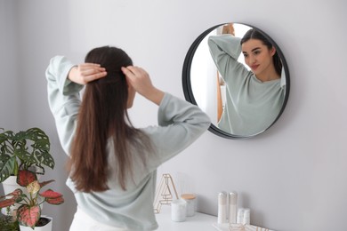 Young woman doing hair near mirror at home. Morning routine