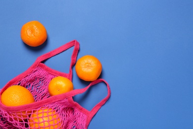 Photo of Pink net bag with citrus fruits on blue background, flat lay. Space for text